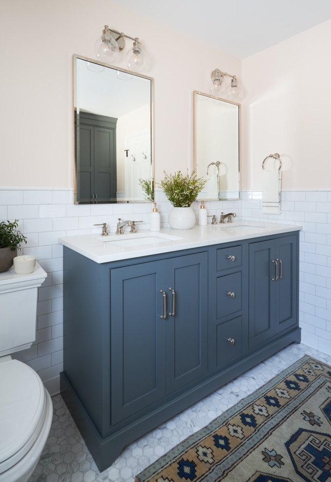 Mid-sized traditional kids bathroom in Chicago with shaker cabinets, blue cabinets, an alcove tub, a shower/bathtub combo, a two-piece toilet, white tile, ceramic tile, pink walls, mosaic tile floors, engineered quartz benchtops, white benchtops, a double vanity and a freestanding vanity.