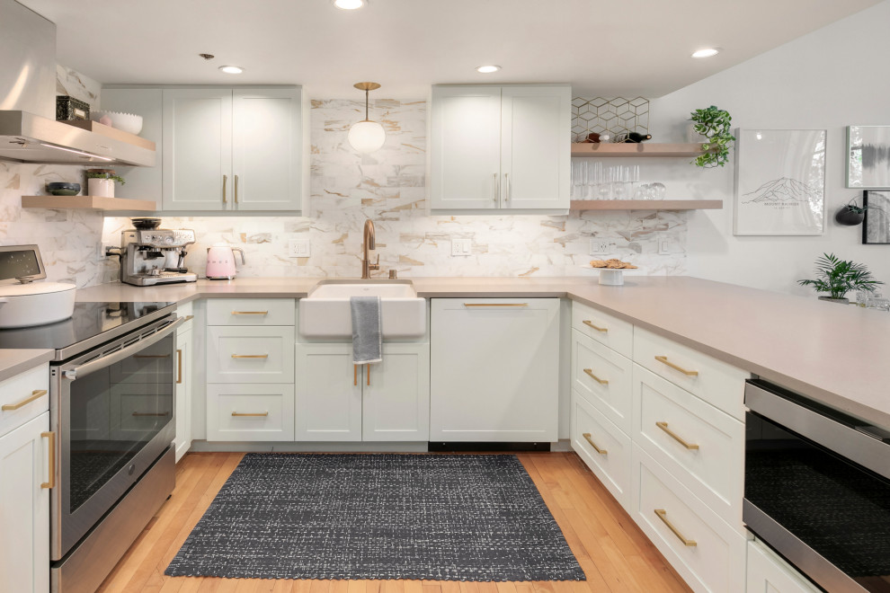 This is an example of a small transitional u-shaped eat-in kitchen in Seattle with a farmhouse sink, shaker cabinets, white cabinets, quartz benchtops, white splashback, marble splashback, stainless steel appliances, light hardwood floors, a peninsula and grey benchtop.