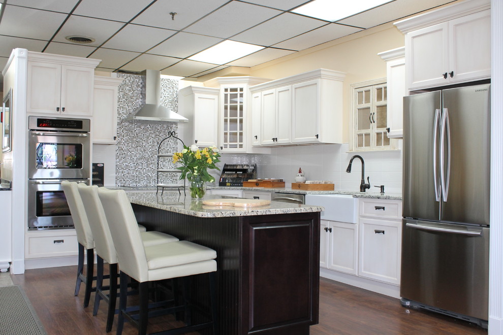 Example of a mid-sized transitional l-shaped dark wood floor kitchen design in Providence with a farmhouse sink, shaker cabinets, white cabinets, granite countertops, multicolored backsplash, mirror backsplash, stainless steel appliances and an island