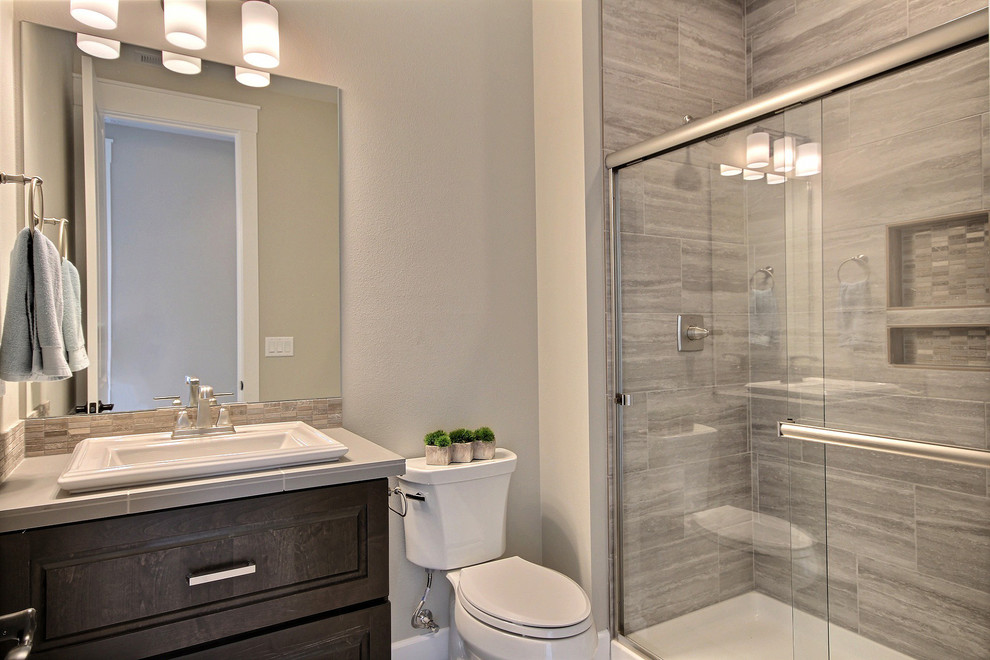 Expansive contemporary kids bathroom in Portland with raised-panel cabinets, dark wood cabinets, an alcove shower, a two-piece toilet, brown tile, ceramic tile, beige walls, porcelain floors, a drop-in sink, tile benchtops, grey floor and a sliding shower screen.