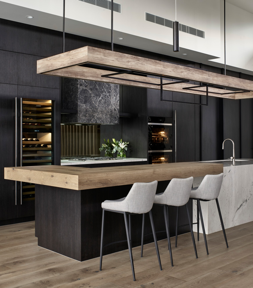Photo of a contemporary galley kitchen in Melbourne with an undermount sink, flat-panel cabinets, black cabinets, black appliances, medium hardwood floors, with island, brown floor and white benchtop.
