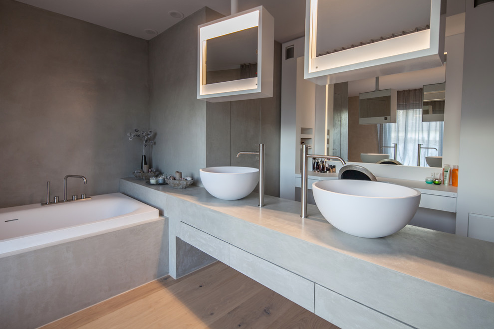 Design ideas for a large contemporary master bathroom in Munich with flat-panel cabinets, white cabinets, a drop-in tub, a wall-mount toilet, gray tile, cement tile, grey walls, light hardwood floors, a vessel sink, concrete benchtops and beige floor.