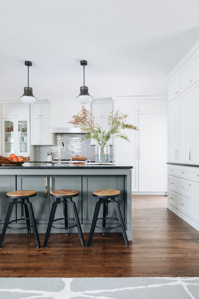 Design ideas for a mid-sized transitional kitchen in Chicago with an undermount sink, shaker cabinets, white cabinets, marble benchtops, grey splashback, ceramic splashback, stainless steel appliances, dark hardwood floors, with island, brown floor and black benchtop.