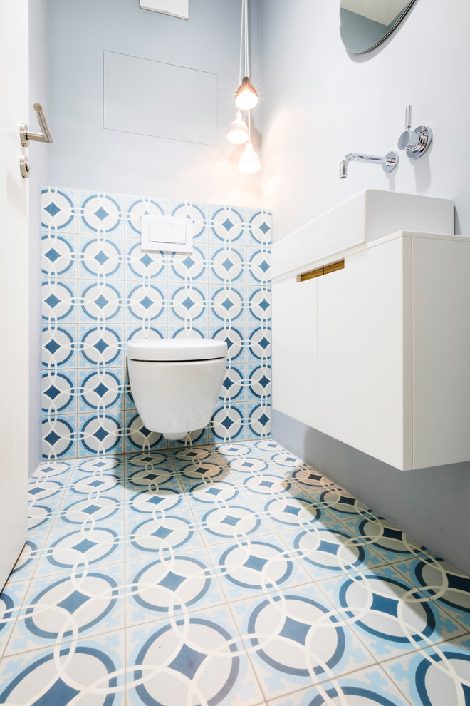 Inspiration for a small contemporary powder room in Munich with flat-panel cabinets, white cabinets, a two-piece toilet, blue tile, white tile, cement tile, grey walls, cement tiles, a vessel sink and multi-coloured floor.