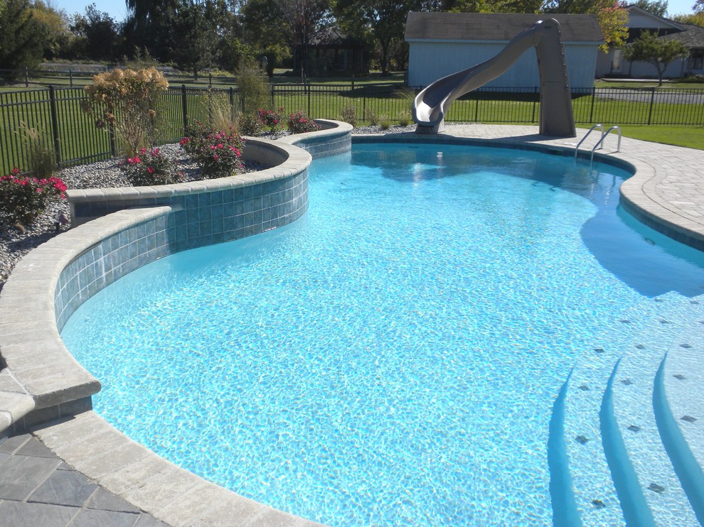 Photo of a mid-sized traditional backyard custom-shaped pool in Other with a water slide and tile.