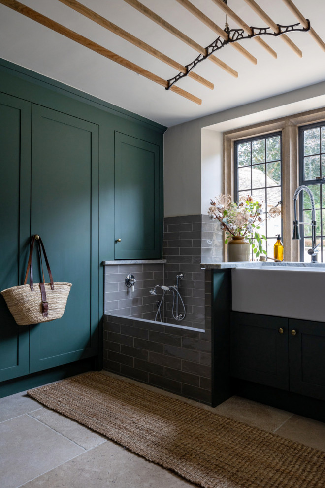 Inspiration for a mid-sized country u-shaped utility room in Gloucestershire with a farmhouse sink, shaker cabinets, green cabinets, granite benchtops, beige walls, limestone floors, a side-by-side washer and dryer, beige floor and multi-coloured benchtop.