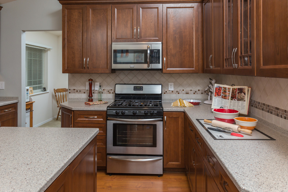 Inspiration for a mid-sized transitional u-shaped medium tone wood floor kitchen pantry remodel with an undermount sink, recessed-panel cabinets, medium tone wood cabinets, solid surface countertops, beige backsplash, mosaic tile backsplash, stainless steel appliances and an island