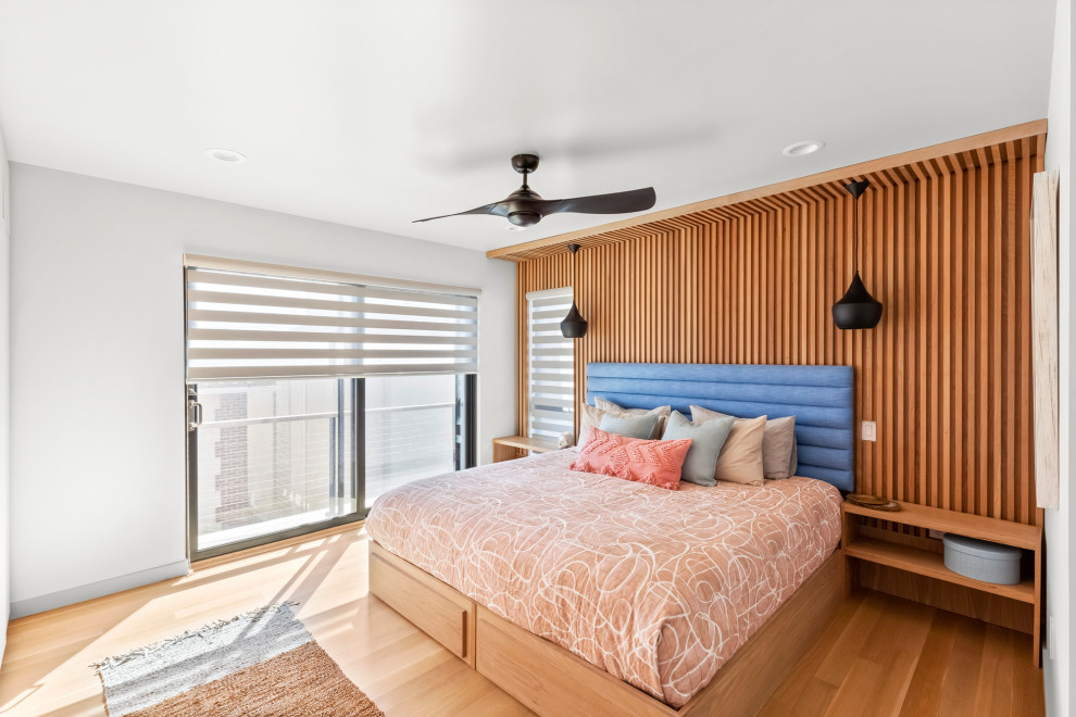 This is an example of a contemporary bedroom in New York with white walls, no fireplace, brown floor and wood walls.