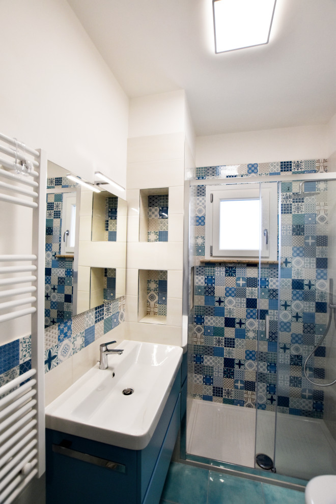 Cette image montre une petite douche en alcôve principale méditerranéenne avec un placard à porte plane, des portes de placard turquoises, WC séparés, un carrelage bleu, des carreaux de porcelaine, un mur blanc, un sol en carrelage de porcelaine, un lavabo suspendu, un sol turquoise, une cabine de douche à porte coulissante, un plan de toilette blanc, une niche, meuble simple vasque et meuble-lavabo suspendu.