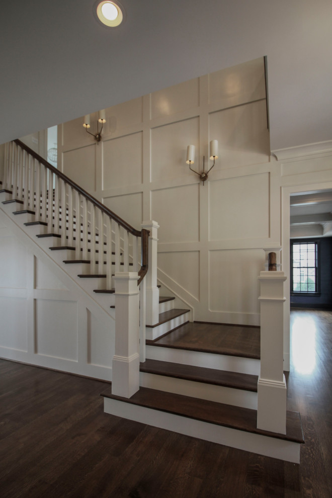 Photo of a large transitional wood u-shaped staircase in DC Metro with wood risers, wood railing and decorative wall panelling.