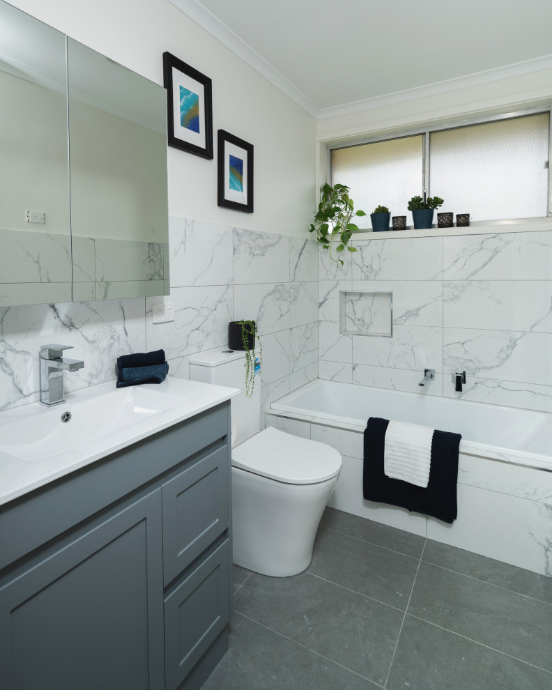 This is an example of a modern bathroom in Melbourne with shaker cabinets, grey cabinets, a drop-in tub, black and white tile, porcelain tile, white walls, porcelain floors, solid surface benchtops, grey floor, white benchtops, a niche, a single vanity and a freestanding vanity.