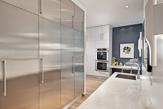 Photo of a mid-sized contemporary galley kitchen pantry in Chicago with a drop-in sink, flat-panel cabinets, stainless steel cabinets, marble benchtops, stainless steel appliances, light hardwood floors and no island.