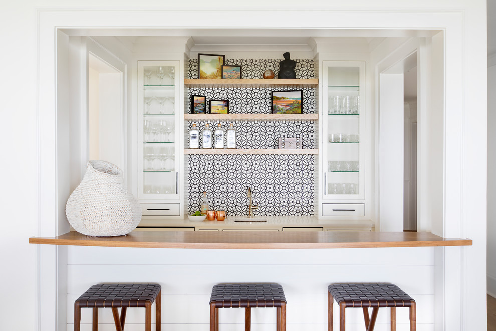 Transitional galley home bar in Charleston with glass-front cabinets, white cabinets, multi-coloured splashback, medium hardwood floors and brown floor.