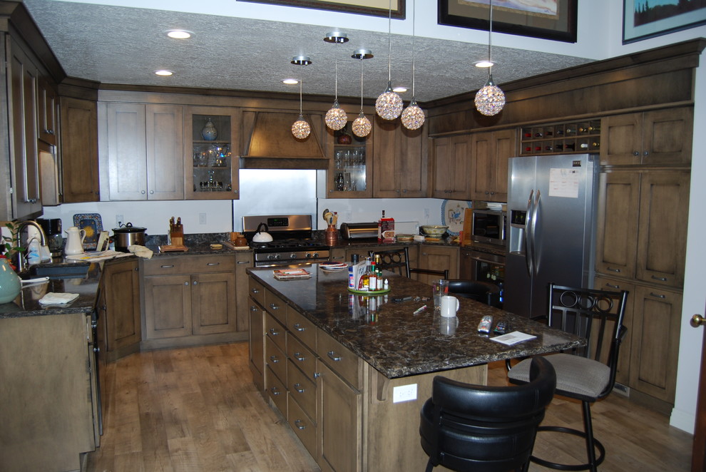 Inspiration for a large transitional u-shaped vinyl floor and brown floor eat-in kitchen remodel with recessed-panel cabinets, brown cabinets, black backsplash, stainless steel appliances, an island, quartz countertops and a double-bowl sink
