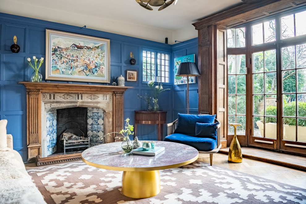 Photo of a large contemporary enclosed living room in London with a library, blue walls, light hardwood floors, a standard fireplace, a stone fireplace surround, a concealed tv, beige floor, wood walls and decorative wall panelling.