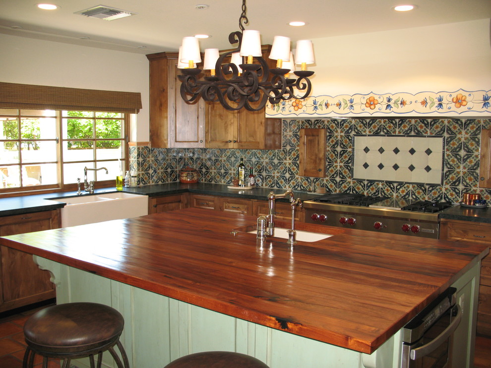 Photo of a large l-shaped eat-in kitchen in Phoenix with a farmhouse sink, recessed-panel cabinets, distressed cabinets, wood benchtops, multi-coloured splashback, terra-cotta splashback, panelled appliances, painted wood floors and with island.