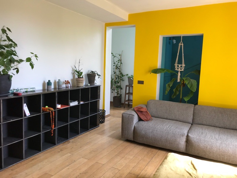 Photo of a mid-sized tropical open concept living room in Paris with a library, yellow walls, light hardwood floors, a wood stove, a metal fireplace surround, a freestanding tv and black floor.
