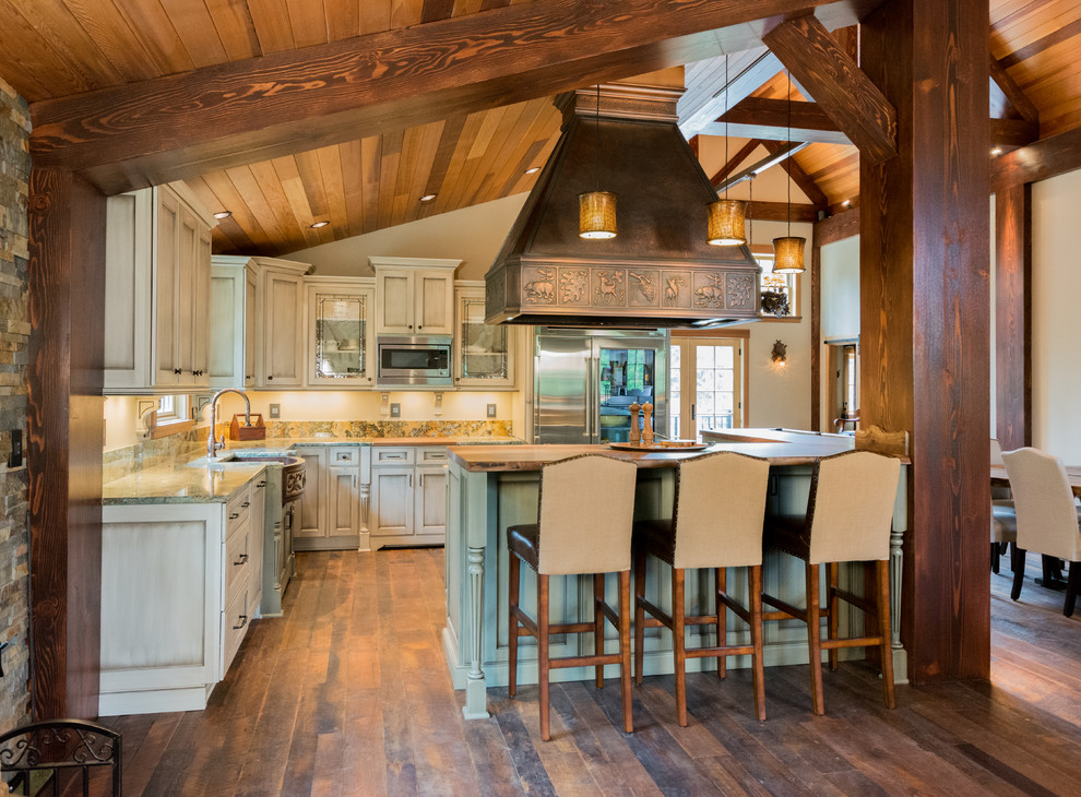 This is an example of a large rustic l-shaped open plan kitchen in Portland with a belfast sink, recessed-panel cabinets, distressed cabinets, granite worktops, stone slab splashback, stainless steel appliances, dark hardwood flooring and an island.