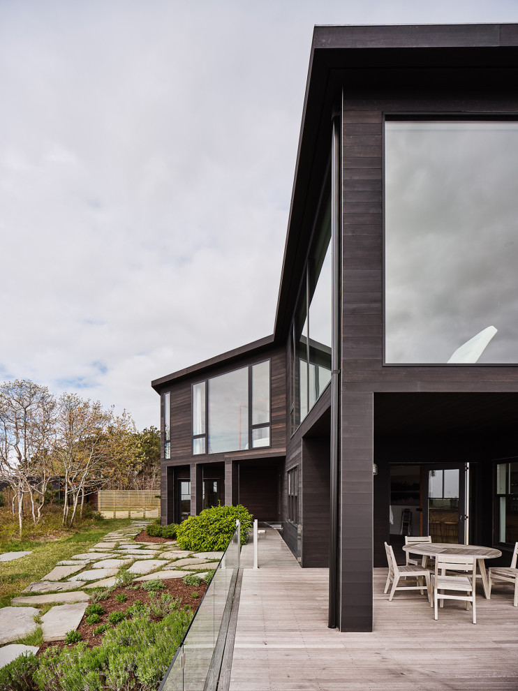 Modern two-storey black house exterior in New York with wood siding, a flat roof and a black roof.