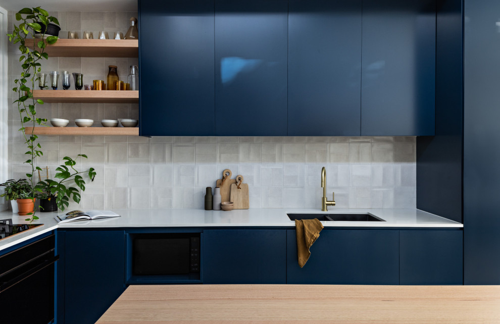 Kleine Moderne Wohnküche in L-Form mit Unterbauwaschbecken, blauen Schränken, Quarzwerkstein-Arbeitsplatte, Küchenrückwand in Weiß, Rückwand aus Keramikfliesen, schwarzen Elektrogeräten, Betonboden, Kücheninsel, grauem Boden und weißer Arbeitsplatte in Sydney
