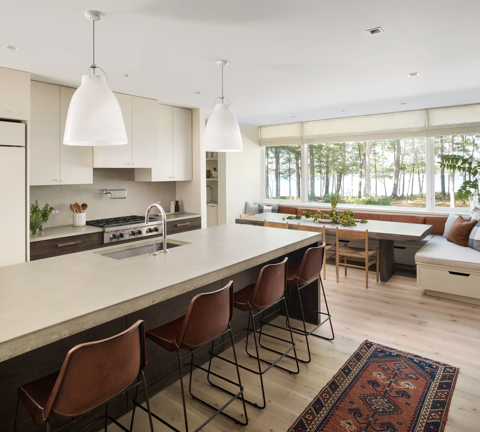 Trendy light wood floor and beige floor eat-in kitchen photo in Portland Maine with an undermount sink, flat-panel cabinets, beige cabinets, beige backsplash, stainless steel appliances, an island and concrete countertops