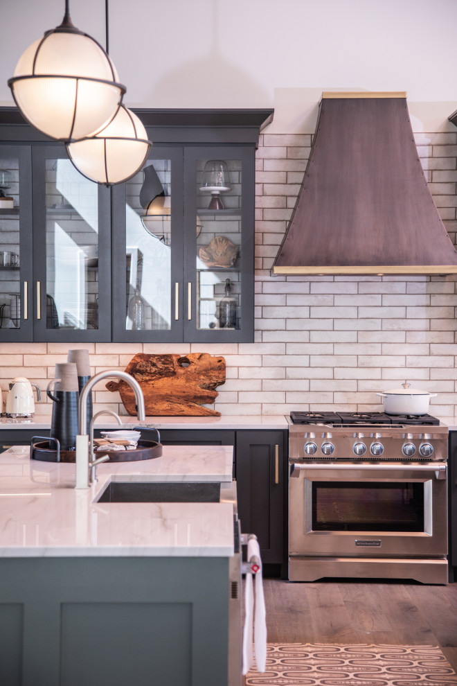 Open concept kitchen - large transitional u-shaped medium tone wood floor and brown floor open concept kitchen idea with a farmhouse sink, shaker cabinets, black cabinets, quartzite countertops, white backsplash, porcelain backsplash, stainless steel appliances, two islands and white countertops