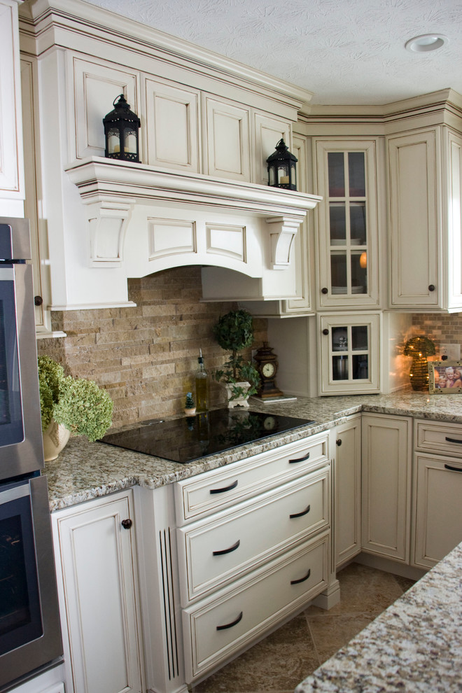 Large u-shaped ceramic tile eat-in kitchen photo with a farmhouse sink, recessed-panel cabinets, distressed cabinets, granite countertops, beige backsplash, stone tile backsplash, stainless steel appliances and an island