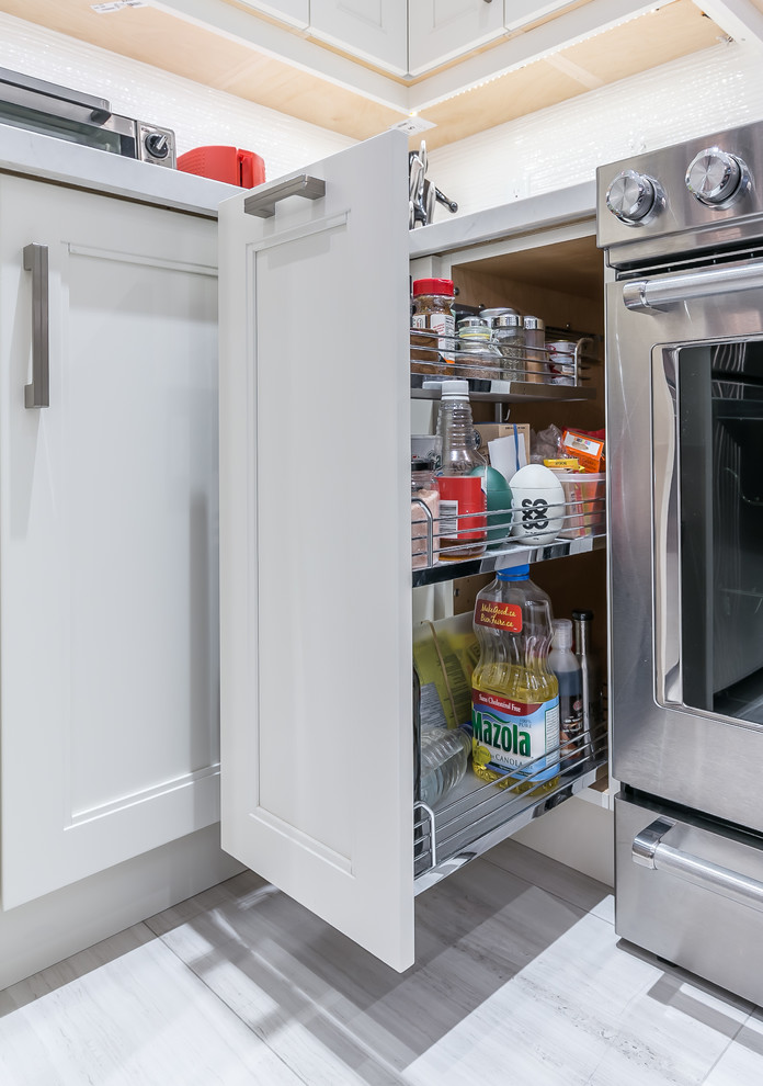 Mid-sized transitional l-shaped porcelain tile eat-in kitchen photo in Toronto with a drop-in sink, recessed-panel cabinets, white cabinets, quartz countertops, stainless steel appliances and an island