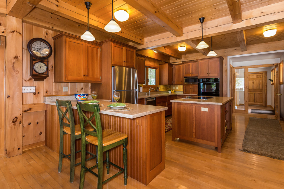 Country u-shaped kitchen in Boston with shaker cabinets, medium wood cabinets, stainless steel appliances, medium hardwood floors, with island and brown floor.
