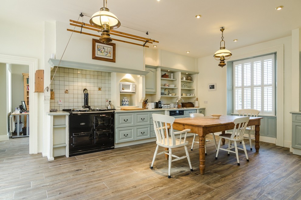 Design ideas for a country eat-in kitchen in Other with raised-panel cabinets, blue cabinets, white splashback, black appliances, dark hardwood floors and subway tile splashback.