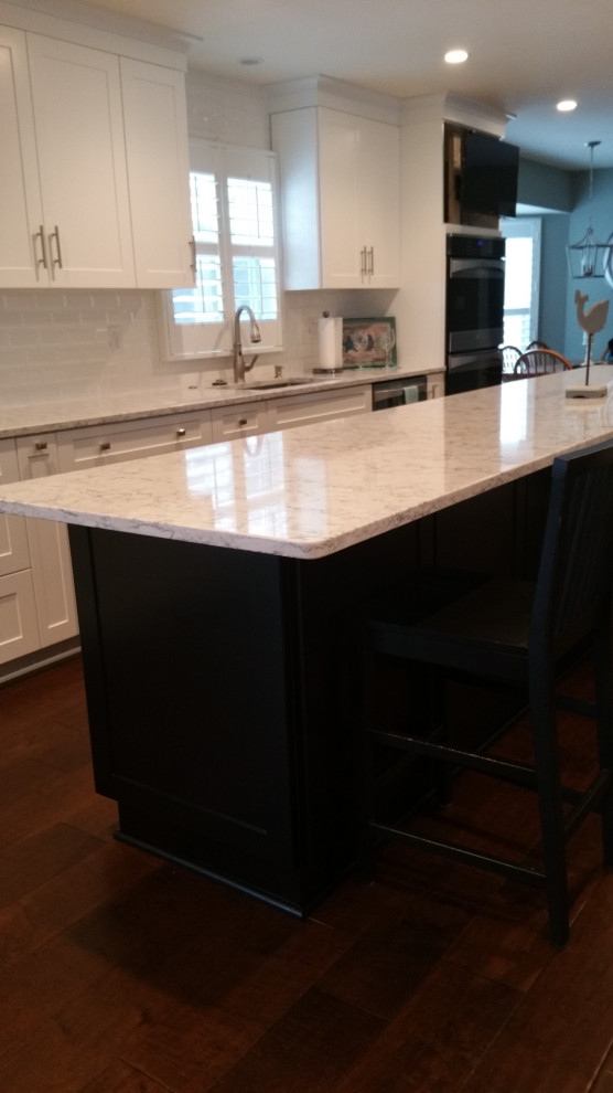 Example of a transitional galley eat-in kitchen design with an undermount sink, shaker cabinets, white cabinets, marble countertops, white backsplash, subway tile backsplash, stainless steel appliances, an island and gray countertops