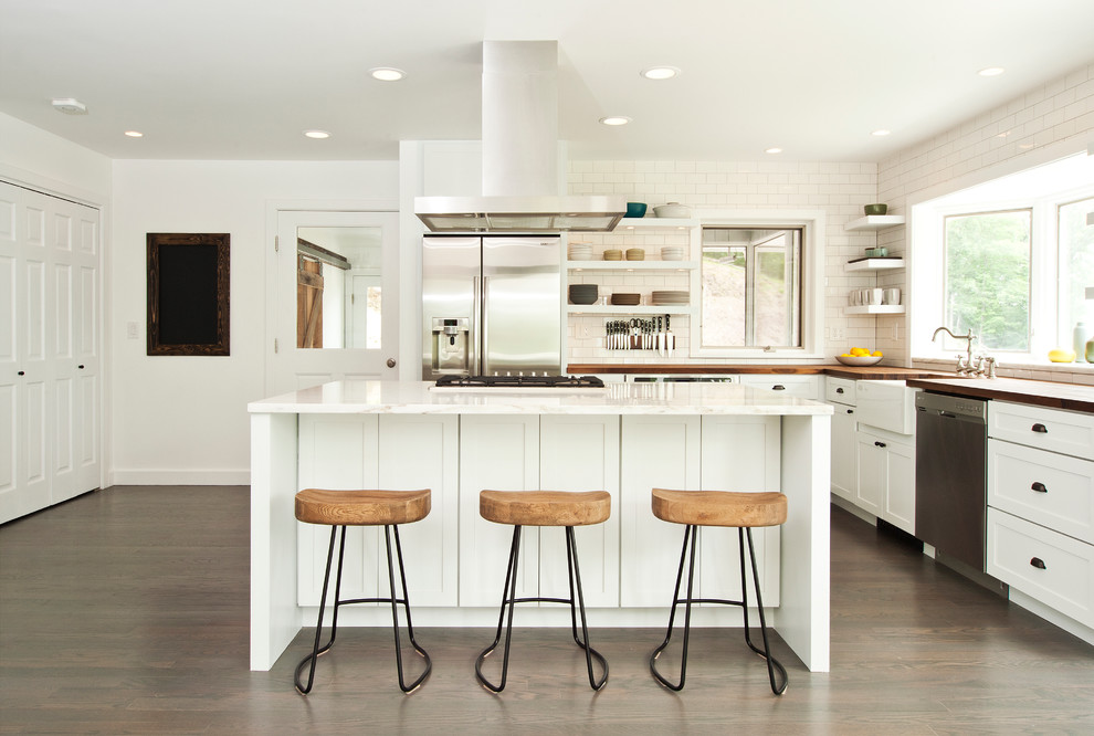 Photo of a transitional l-shaped kitchen in New York with a farmhouse sink, shaker cabinets, white cabinets, white splashback, subway tile splashback, dark hardwood floors and with island.