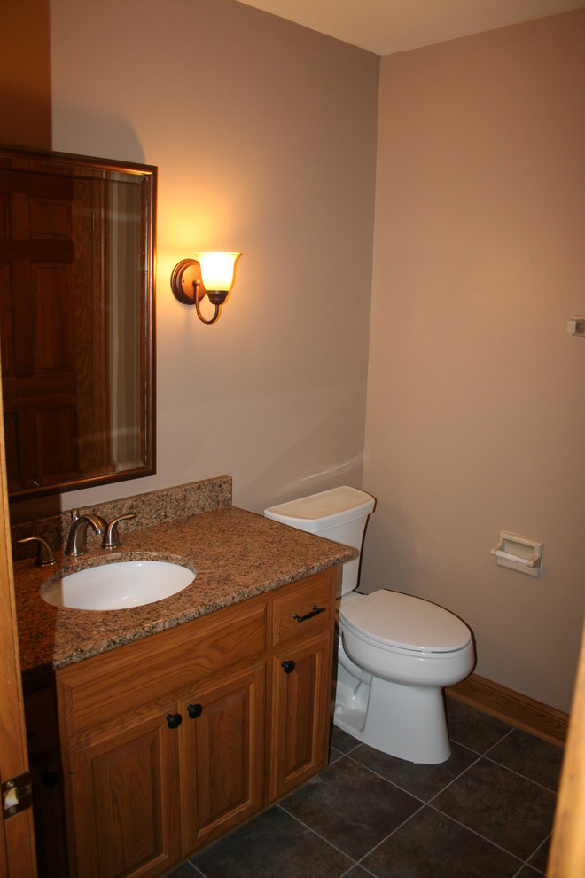 Country powder room in Milwaukee with an undermount sink, raised-panel cabinets, granite benchtops, beige walls, ceramic floors and medium wood cabinets.