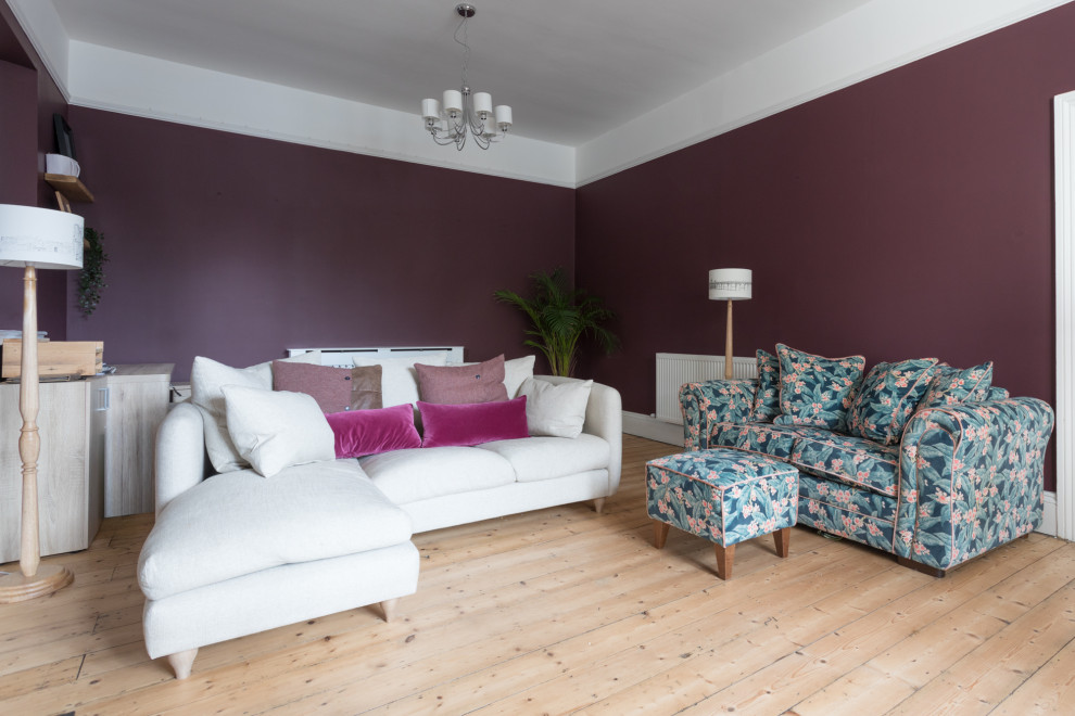 Large victorian enclosed living room with a reading nook, purple walls, light hardwood flooring, a standard fireplace, a stone fireplace surround, a freestanding tv and beige floors.
