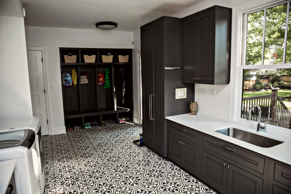 Photo of a large transitional galley dedicated laundry room in Chicago with a single-bowl sink, shaker cabinets, grey cabinets, solid surface benchtops, white walls, ceramic floors and a side-by-side washer and dryer.