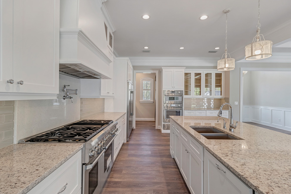 Large country single-wall eat-in kitchen in Jacksonville with a double-bowl sink, shaker cabinets, white cabinets, granite benchtops, beige splashback, glass tile splashback, stainless steel appliances, vinyl floors, with island, brown floor and beige benchtop.