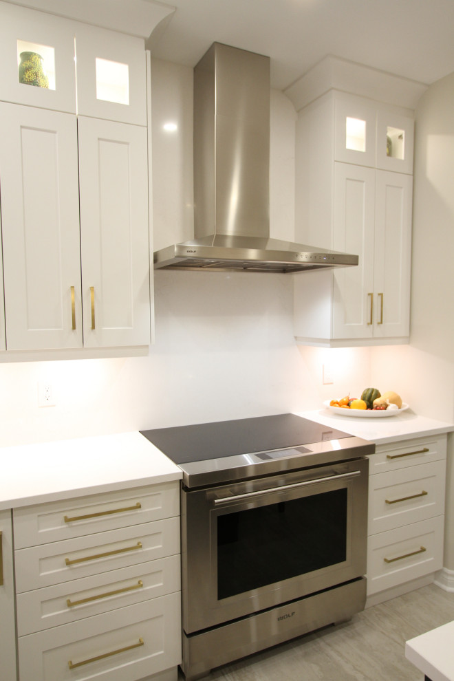 Photo of a large contemporary u-shaped eat-in kitchen in Toronto with an undermount sink, recessed-panel cabinets, white cabinets, quartz benchtops, white splashback, engineered quartz splashback, stainless steel appliances, porcelain floors, with island, grey floor and white benchtop.