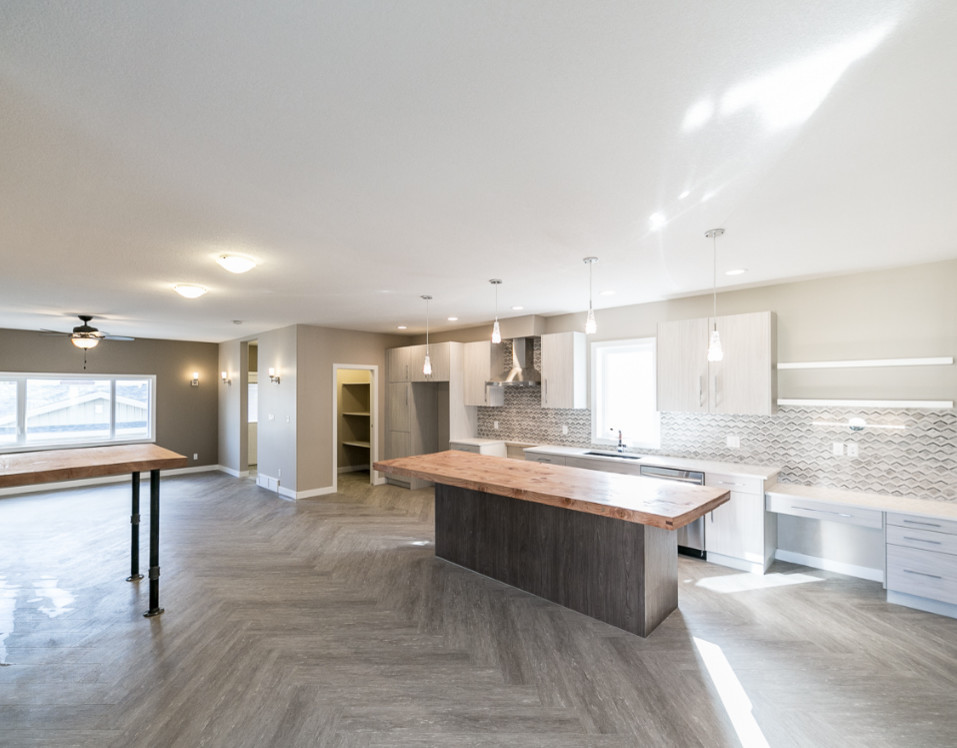 Open concept kitchen - large transitional galley vinyl floor open concept kitchen idea in Edmonton with an undermount sink, flat-panel cabinets, distressed cabinets, wood countertops, multicolored backsplash, stainless steel appliances, an island and porcelain backsplash