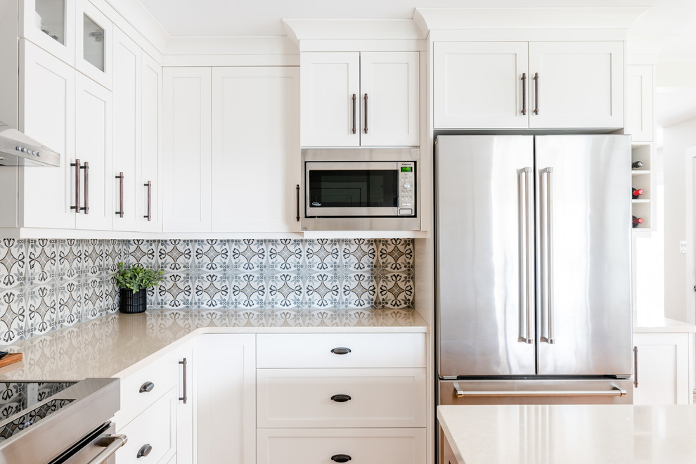 Kitchen pantry - mid-sized transitional l-shaped medium tone wood floor and brown floor kitchen pantry idea with an undermount sink, shaker cabinets, white cabinets, quartzite countertops, gray backsplash, porcelain backsplash, stainless steel appliances, an island and white countertops