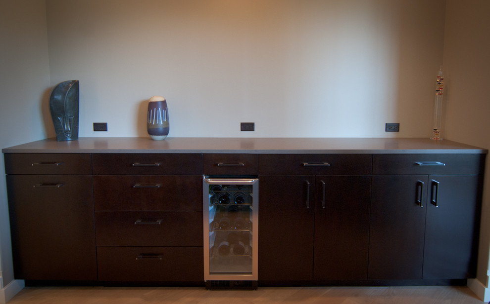 This is an example of a small contemporary galley home bar in Grand Rapids with flat-panel cabinets, black cabinets, quartz benchtops, light hardwood floors, orange floor and grey benchtop.