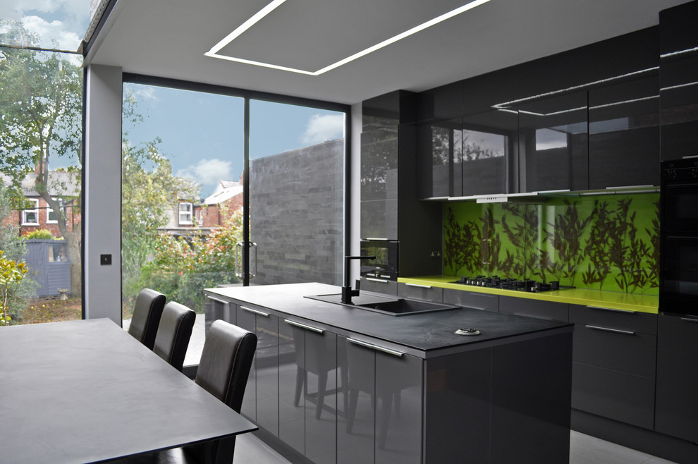 Photo of a contemporary galley eat-in kitchen in London with a drop-in sink, flat-panel cabinets, black cabinets, green splashback and black appliances.