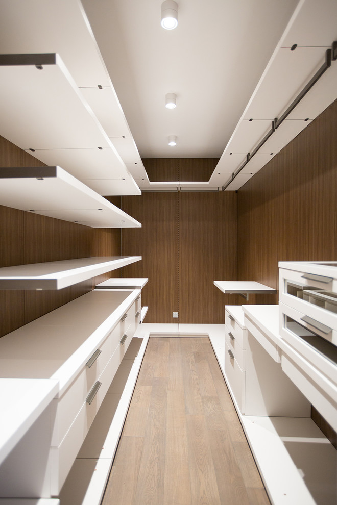 This is an example of a contemporary gender-neutral walk-in wardrobe in Moscow with flat-panel cabinets, white cabinets, light hardwood floors and beige floor.