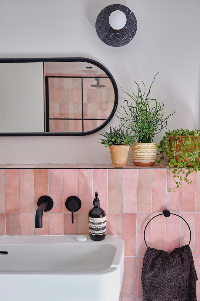 Photo of a mid-sized contemporary kids bathroom in London with black cabinets, an open shower, a wall-mount toilet, pink tile, ceramic tile, white walls, terrazzo floors, a trough sink, black floor, an open shower, a niche and a single vanity.