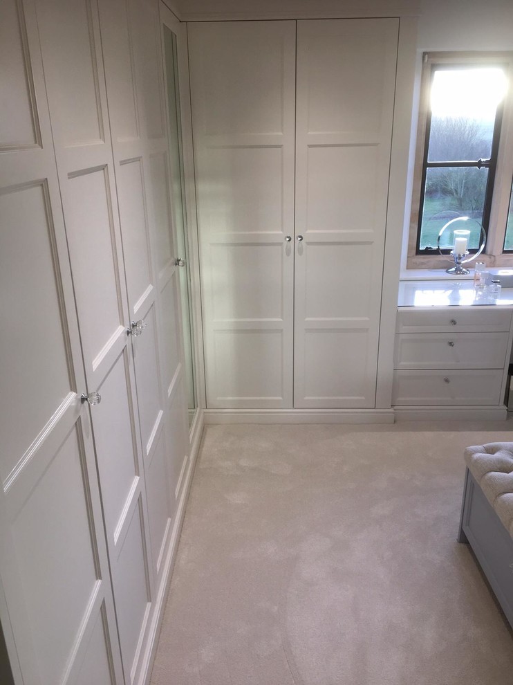 This is an example of a large modern women's dressing room in Gloucestershire with shaker cabinets, white cabinets, carpet and beige floor.