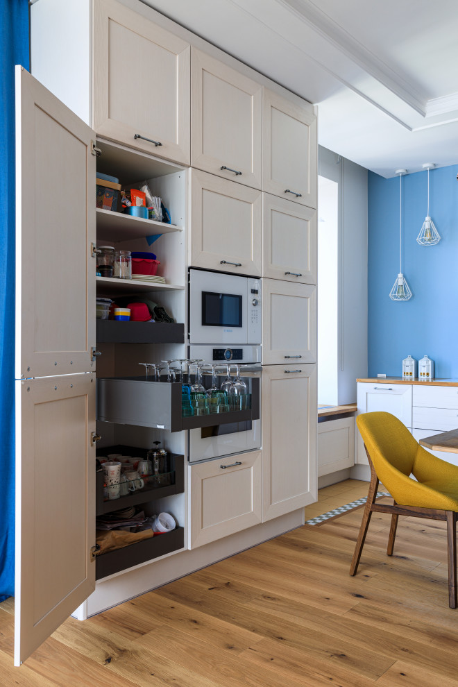 This is an example of a large scandinavian galley eat-in kitchen in Moscow with a drop-in sink, recessed-panel cabinets, white cabinets, wood benchtops, blue splashback, white appliances, medium hardwood floors, no island, brown floor and beige benchtop.