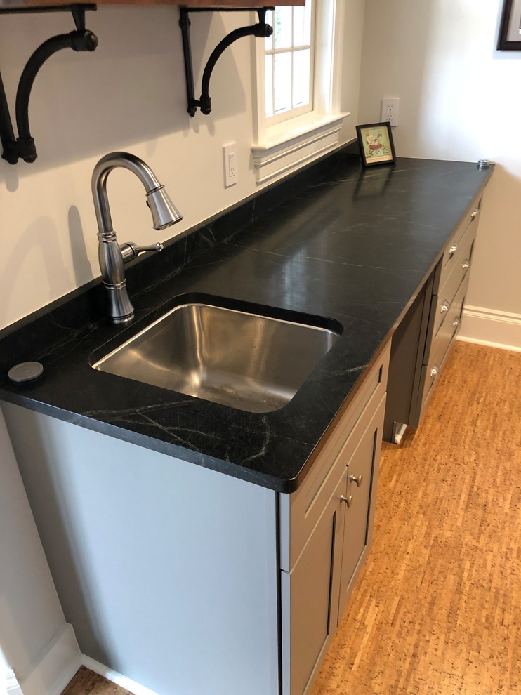 Photo of a mid-sized contemporary single-wall home bar in Philadelphia with a drop-in sink, grey cabinets, granite benchtops, cork floors, brown floor and black benchtop.