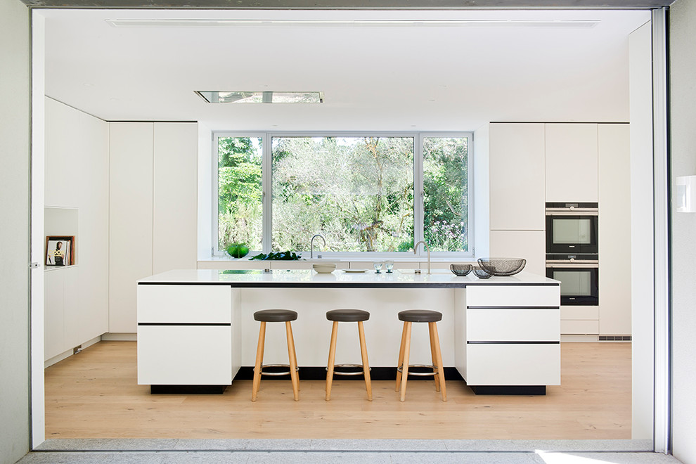 Photo of a large contemporary single-wall kitchen in Madrid with flat-panel cabinets, white cabinets, quartz benchtops, medium hardwood floors, with island and beige floor.