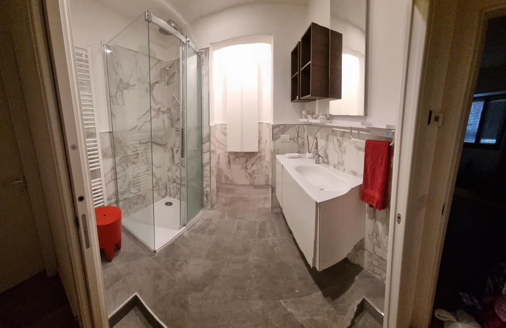 Inspiration för mellanstora moderna vitt badrum med dusch, med vita skåp, en vägghängd toalettstol, porslinskakel, vita väggar, klinkergolv i porslin, bänkskiva i glas, grått golv och dusch med skjutdörr