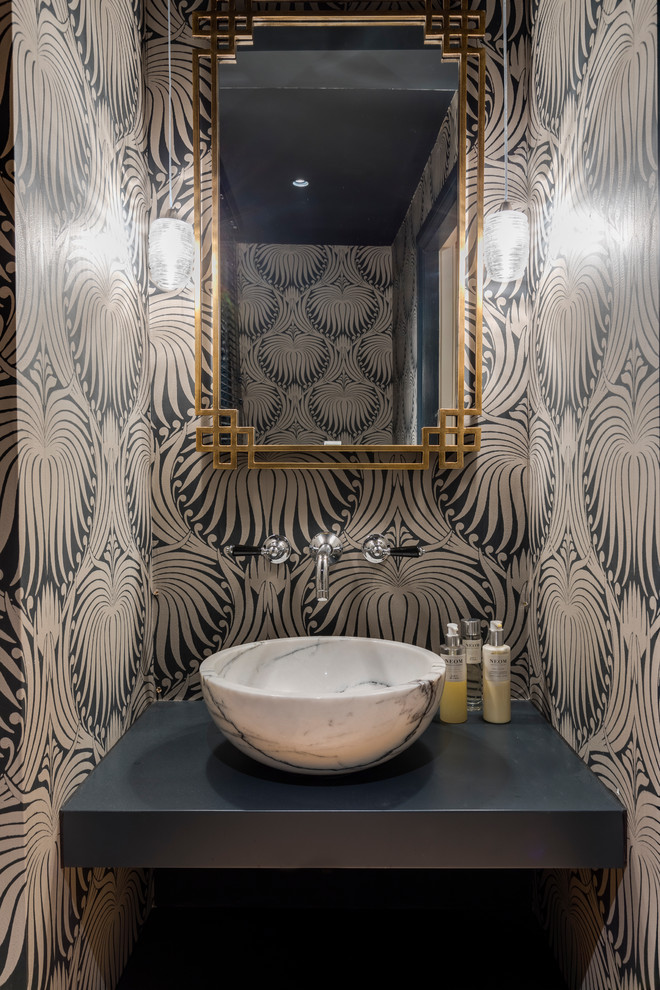 Eclectic powder room in London with a vessel sink, multi-coloured walls and black benchtops.