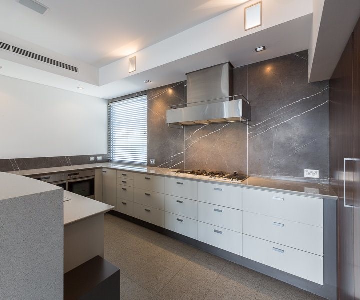 Photo of a mid-sized l-shaped kitchen in Perth with flat-panel cabinets, ceramic floors, a drop-in sink, white cabinets, limestone benchtops, beige splashback, ceramic splashback, stainless steel appliances, with island and beige floor.